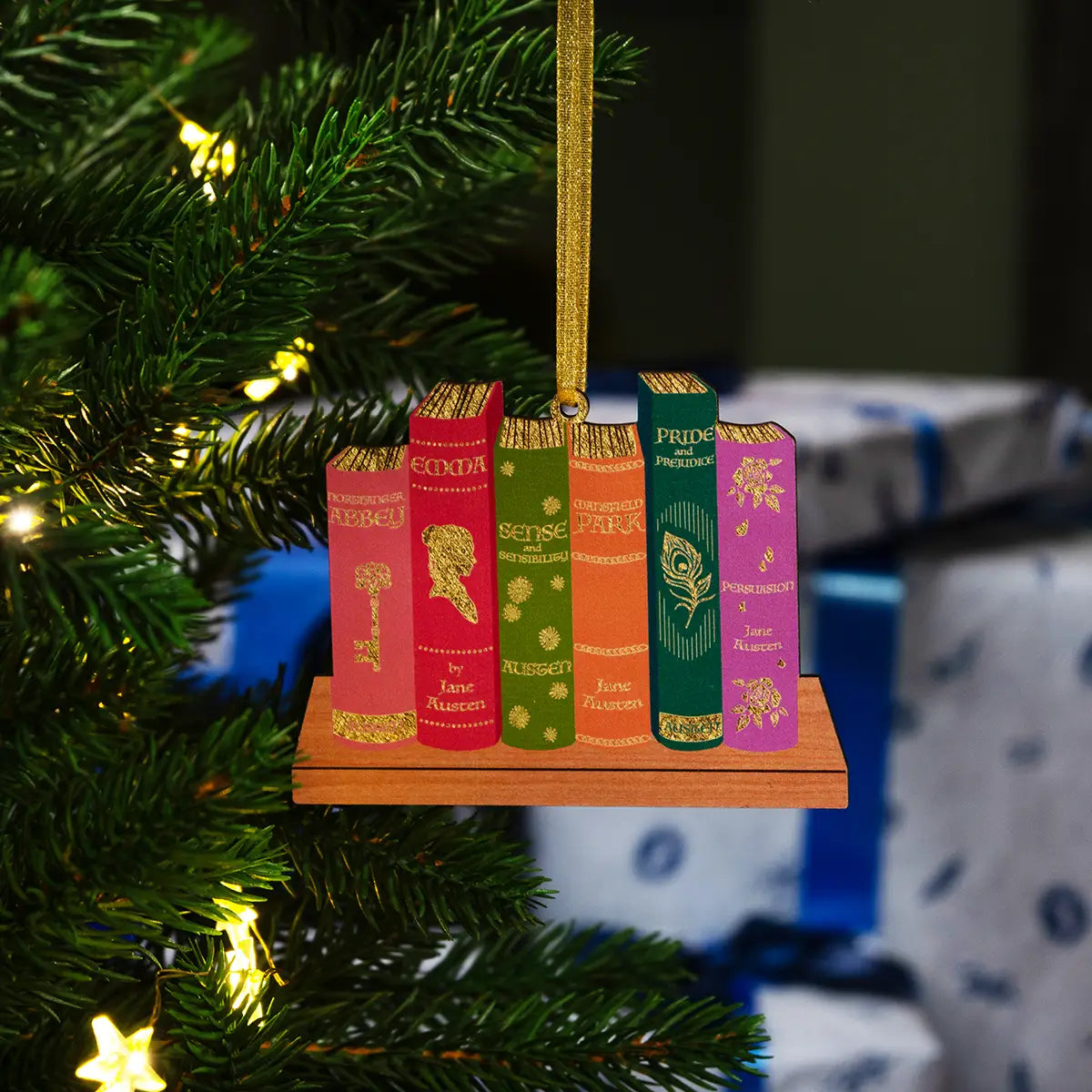 Jane Austen bookshelf decoration hanging from a christmas tree in front of a pile of wrapped christmas presents
