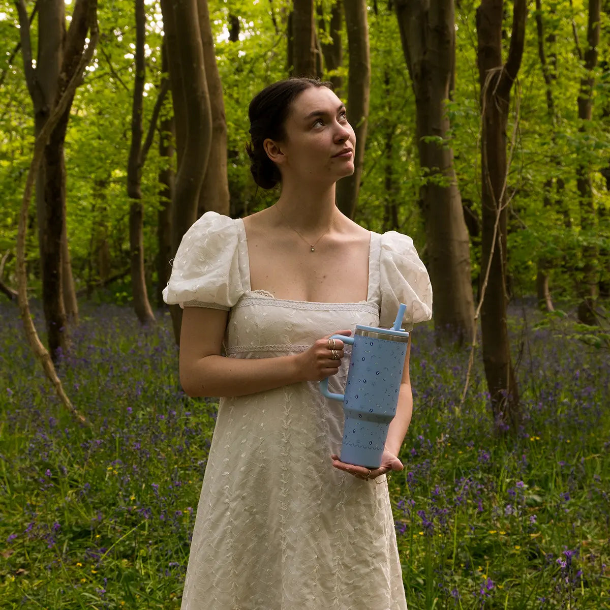 A woman in the woods with a blue Jane Austen themed tumbler