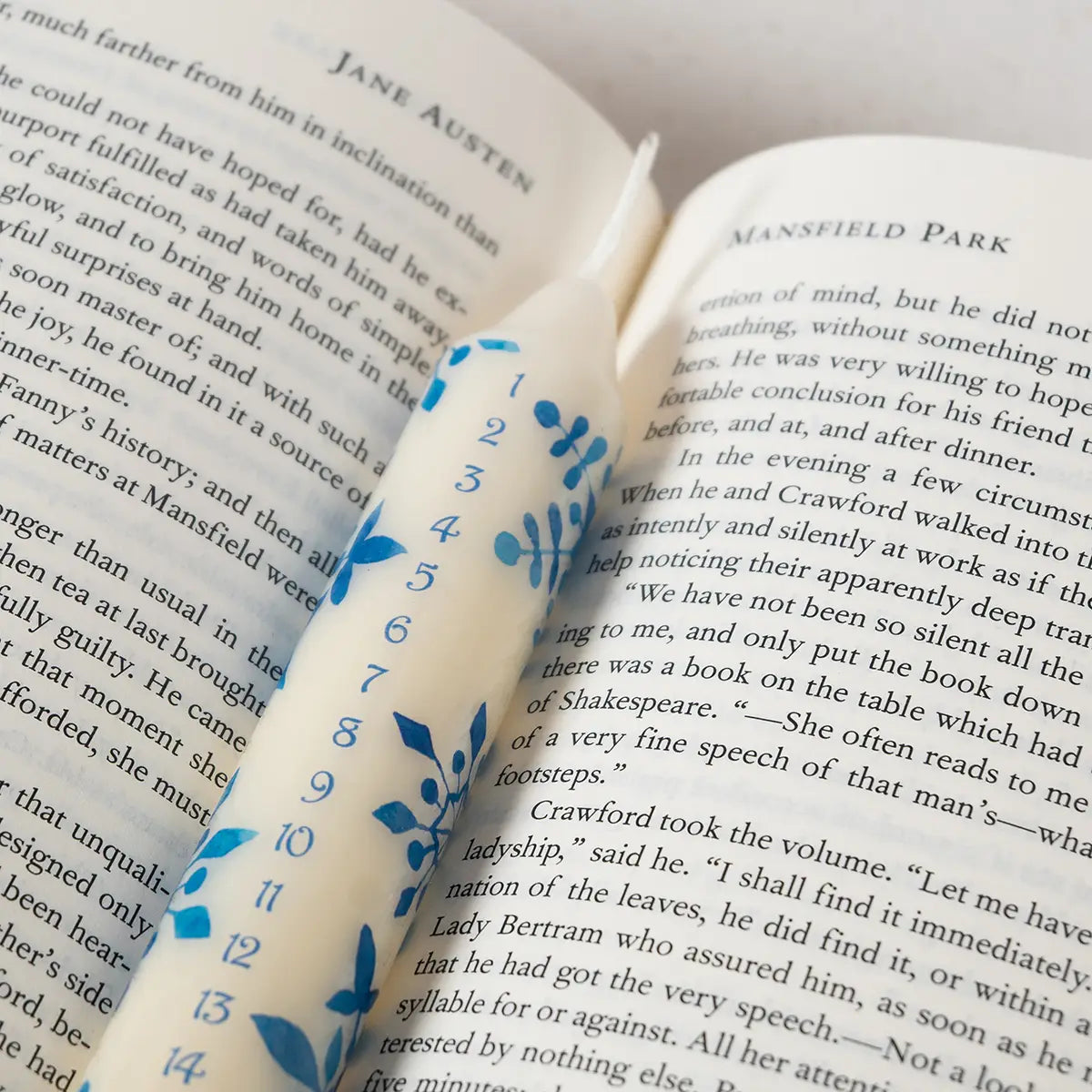 A white advent candle with light blue Jane Austen themed patterns and numbers on an open copy of Mansfield Park by Jane Austen