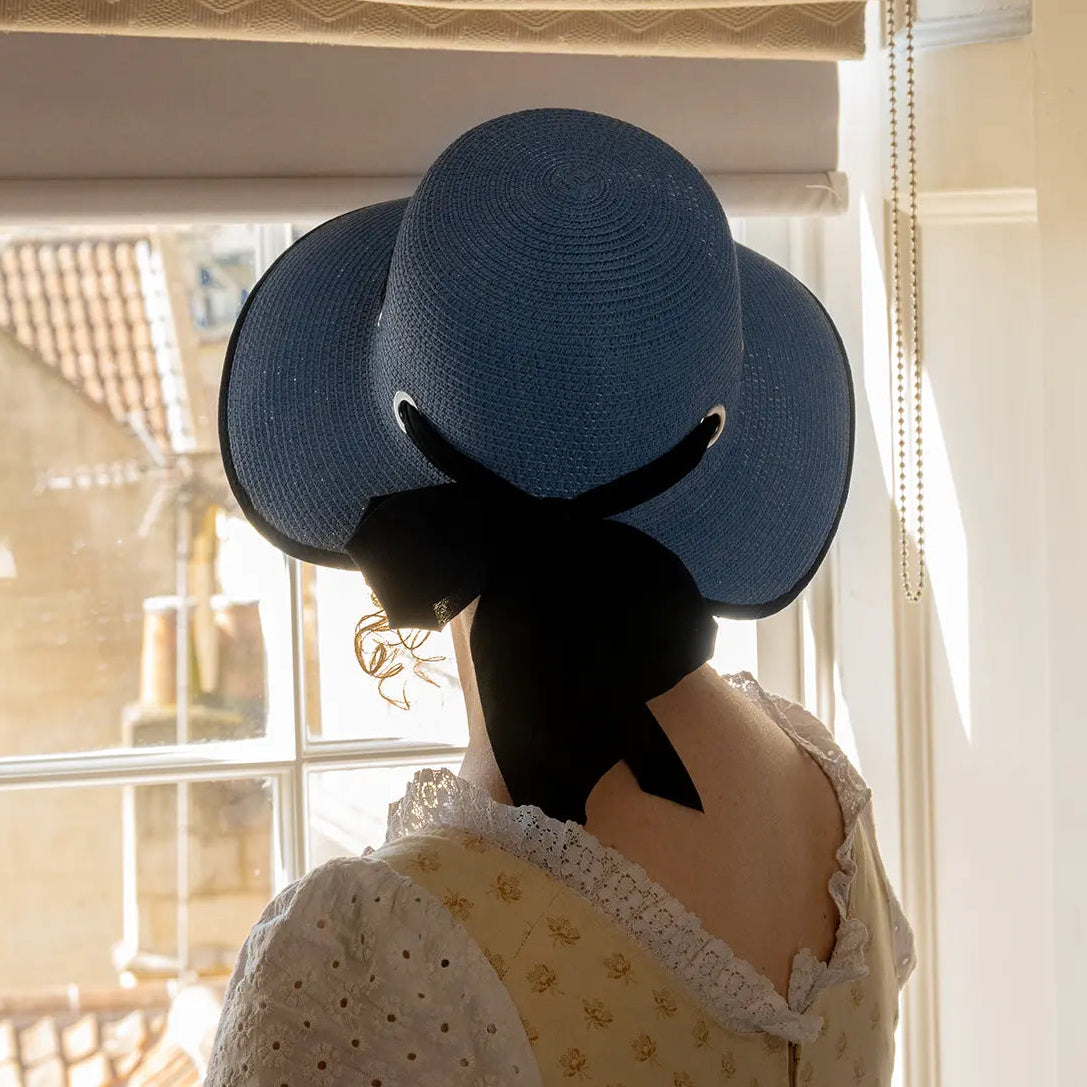 photograph of model looking out of a window while wearing blue open-back regency bonnet