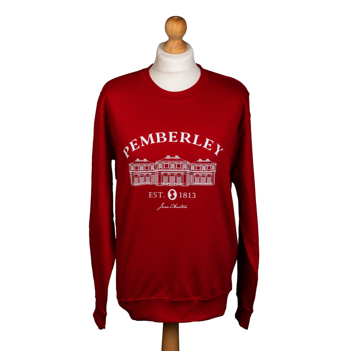red sweater with 'PEMBERLEY EST. 1813 Jane Austen' printed on it in white, on wooden mannequin, against a white background