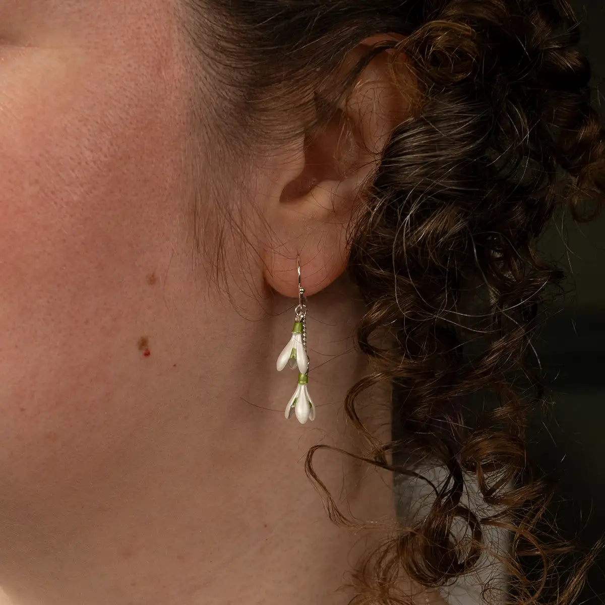 Close-up of an ear wearing a snowdrop earring, with a dark background