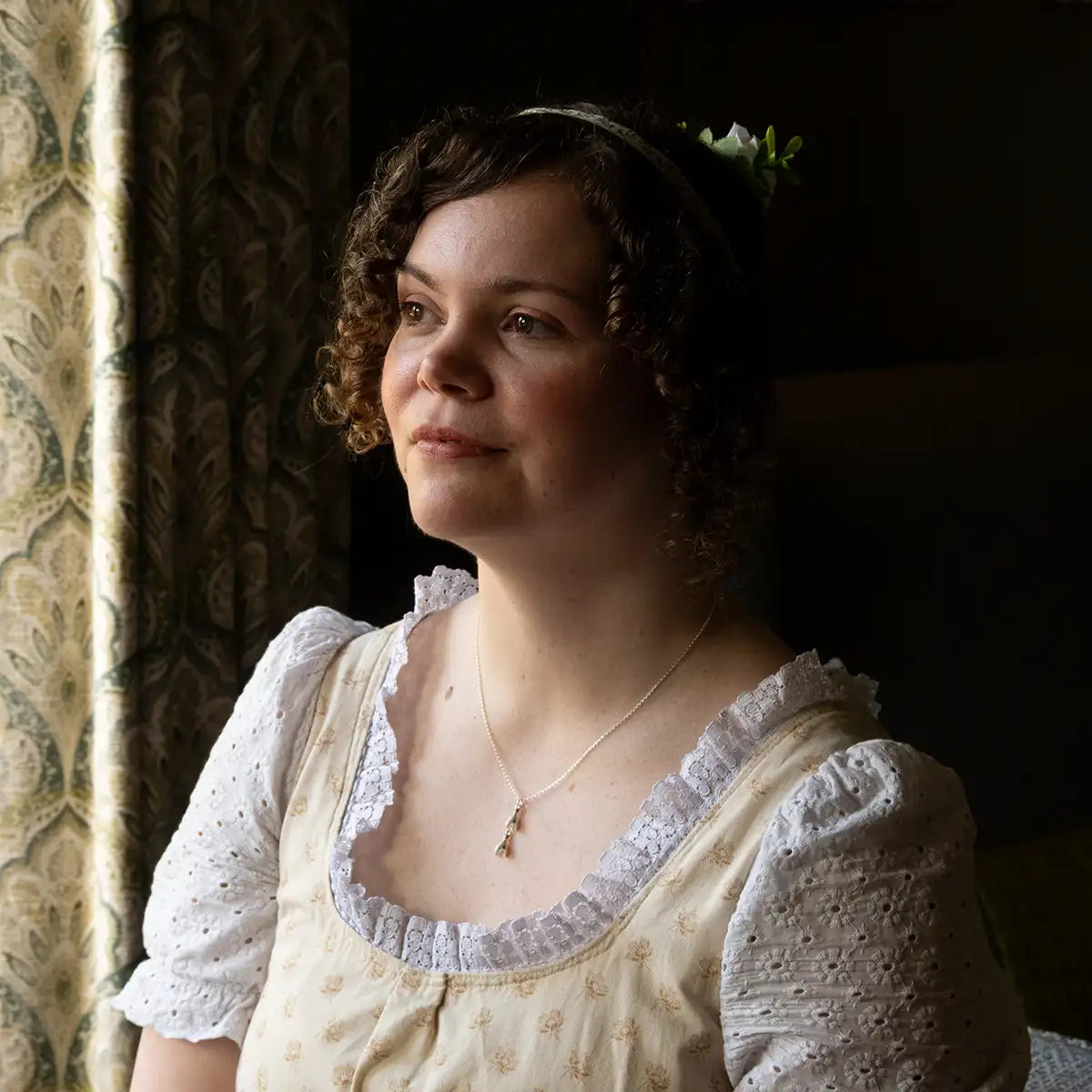 Woman in a historical costume wearing a snowdrop necklace, against a dark background