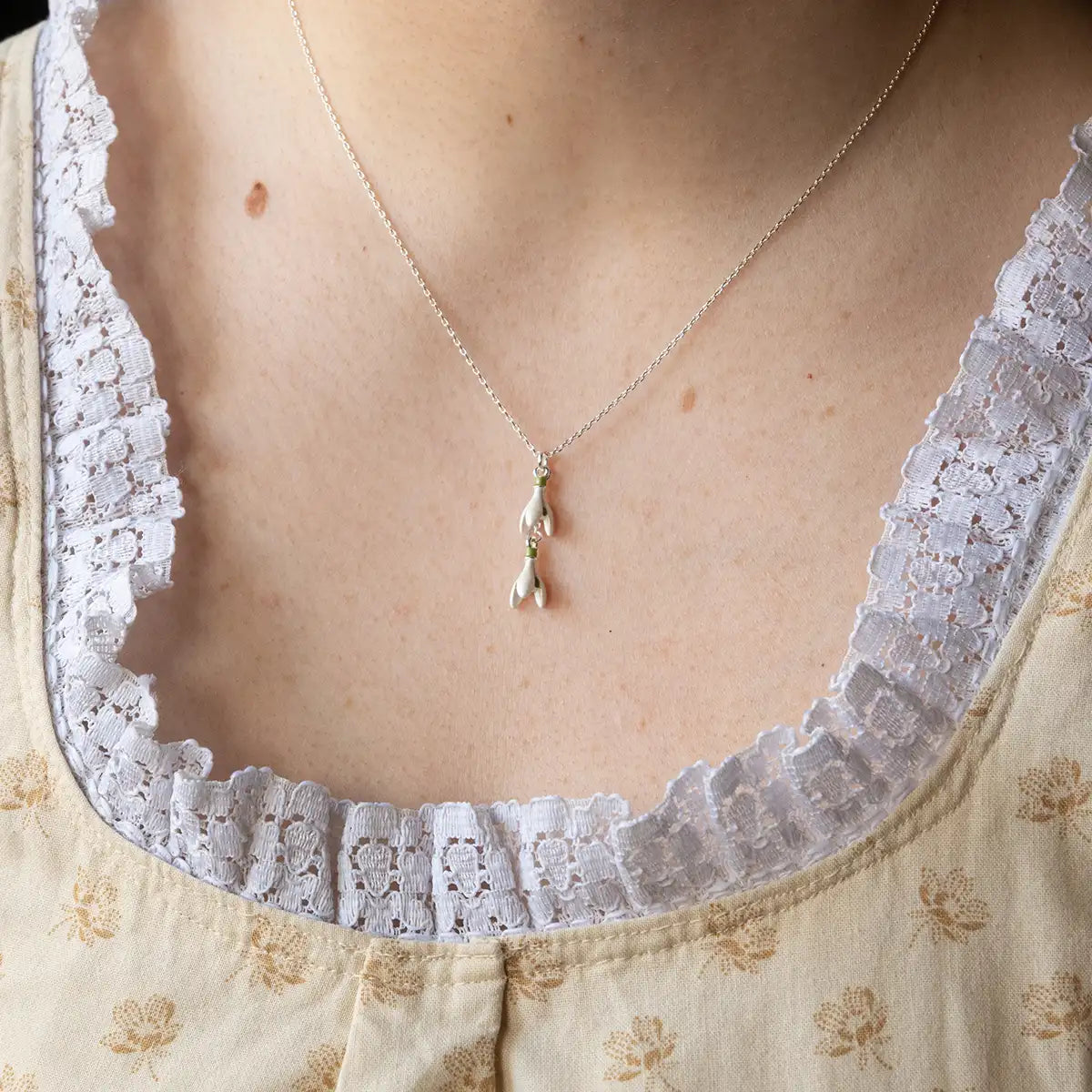 Necklace with a  snowdrop pendant worn by a person wearing a lace-trimmed garment.