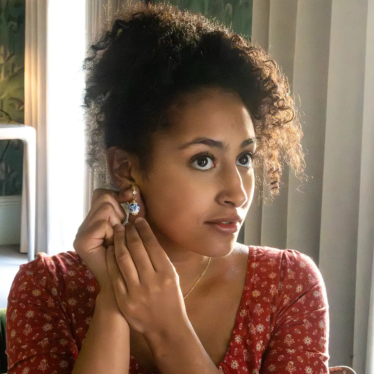 Woman adjusting an earring indoors with a neutral background