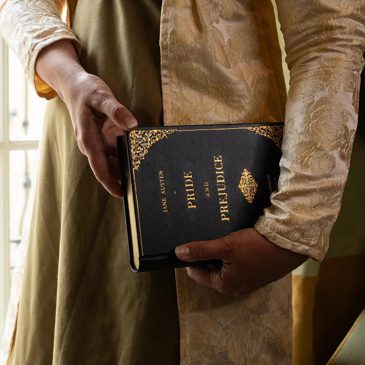 A woman in regency attire holding the Pride and Prejudice Book Clutch Navy next to a window