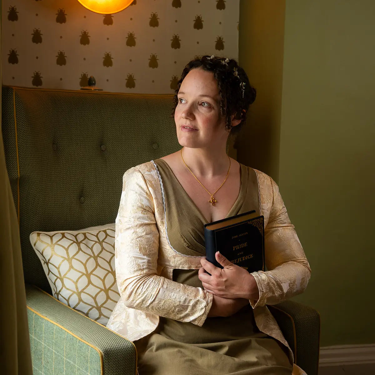 A woman in regency attire sat in a chair clutching the pride and prejudice book clutch bag navy