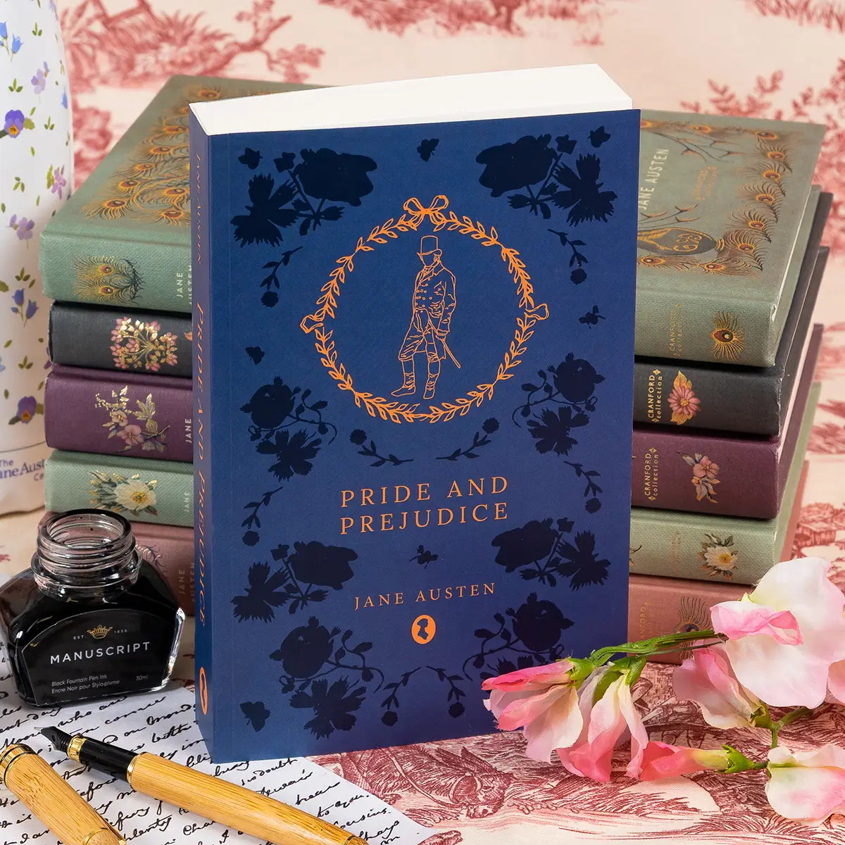 Jane Austen Centre edition of Pride and Prejudice by Jane Austen on a tableaux with books, flowers, ink, pens, and letters