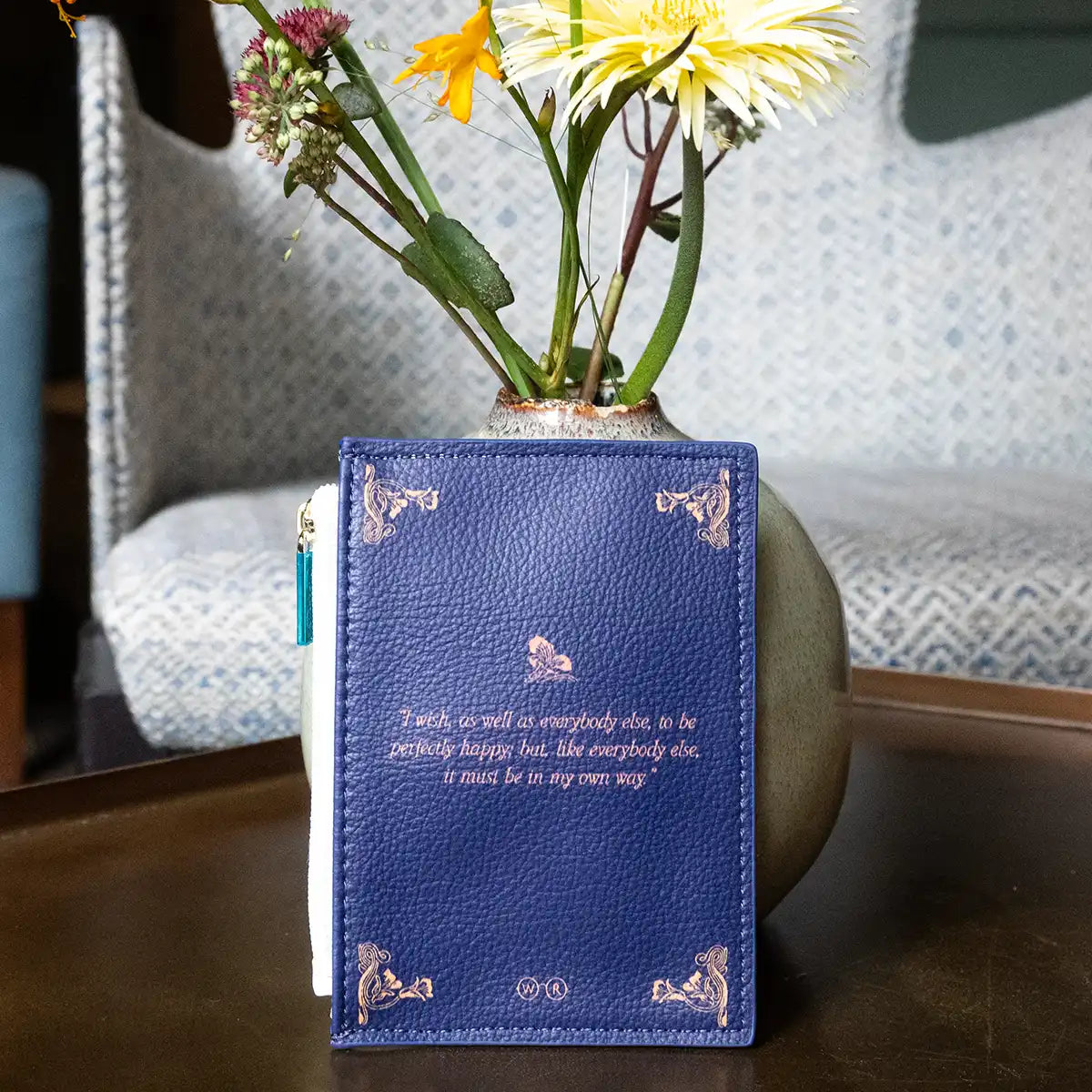 Blue coin purse with decorative cover and floral arrangement on a surface.