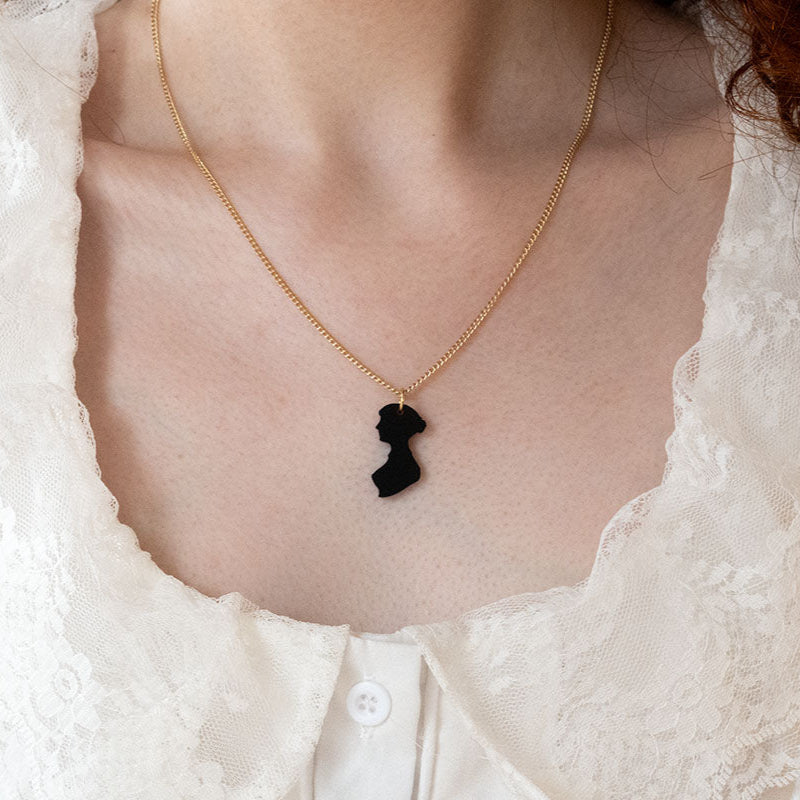 Black acrylic necklace on a gold chain on the neck of a woman in the shape of Jane Austen's silhouette