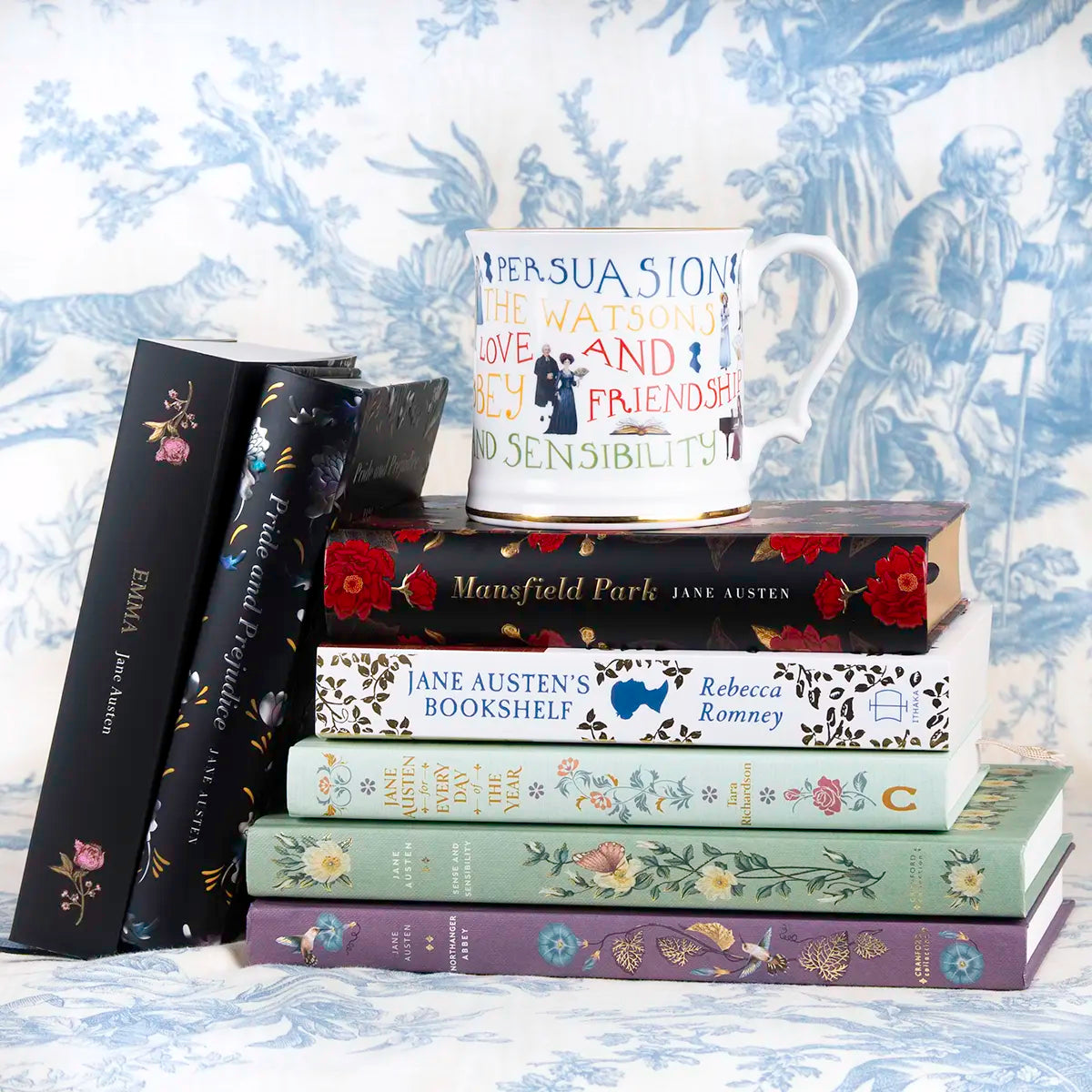 Jane Austen themed mug with gold trim on top of a stack of Jane Austen's books, against a blue background
