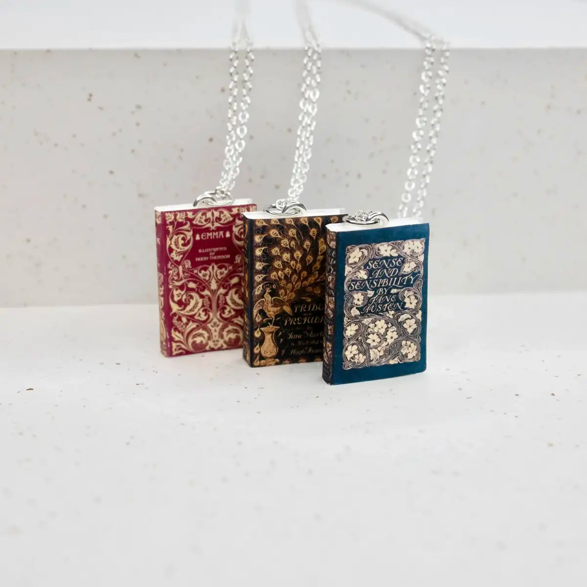 three book page necklaces on smooth stone background