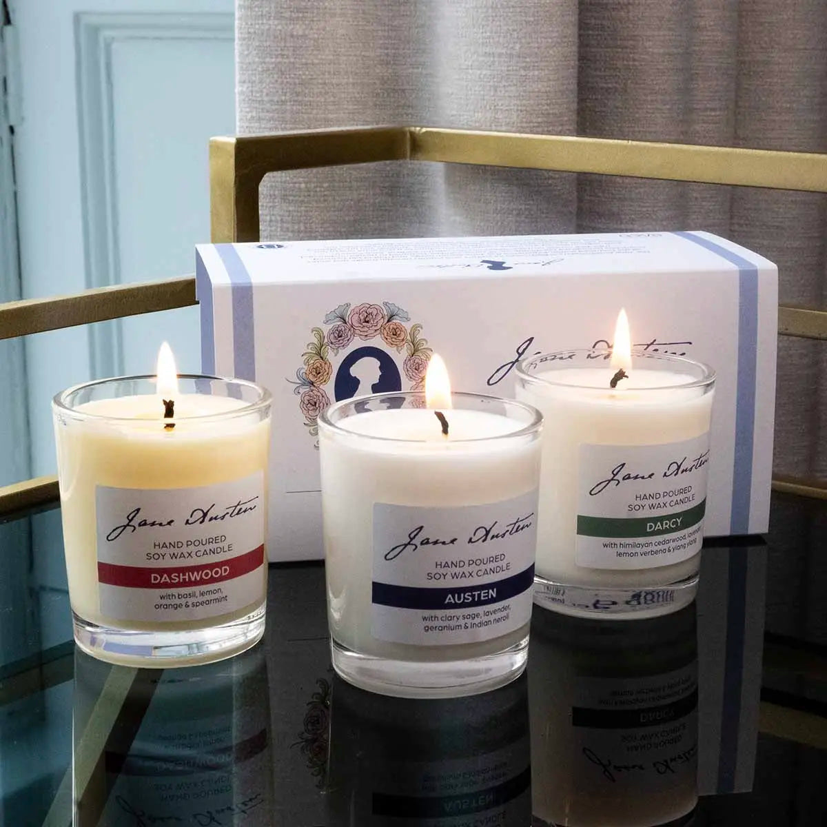 Three candles 'Darcy', 'Austen' and 'Dashwood' lit on a gold edged table.