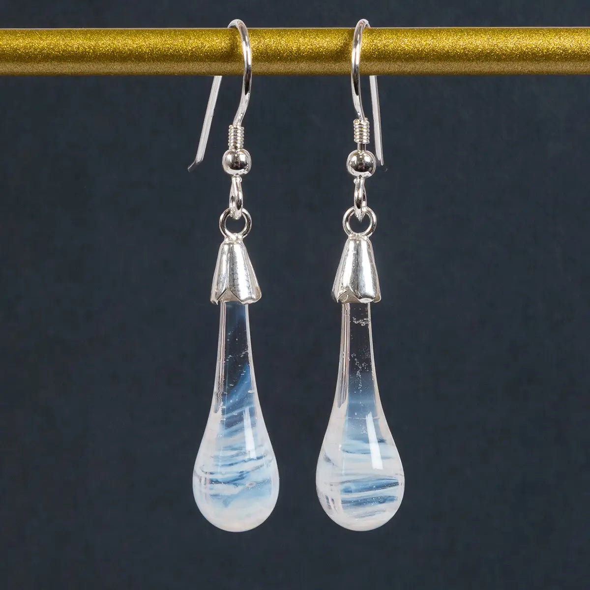 white glass drop earrings with silver details hanging in front of a black wibalin background
