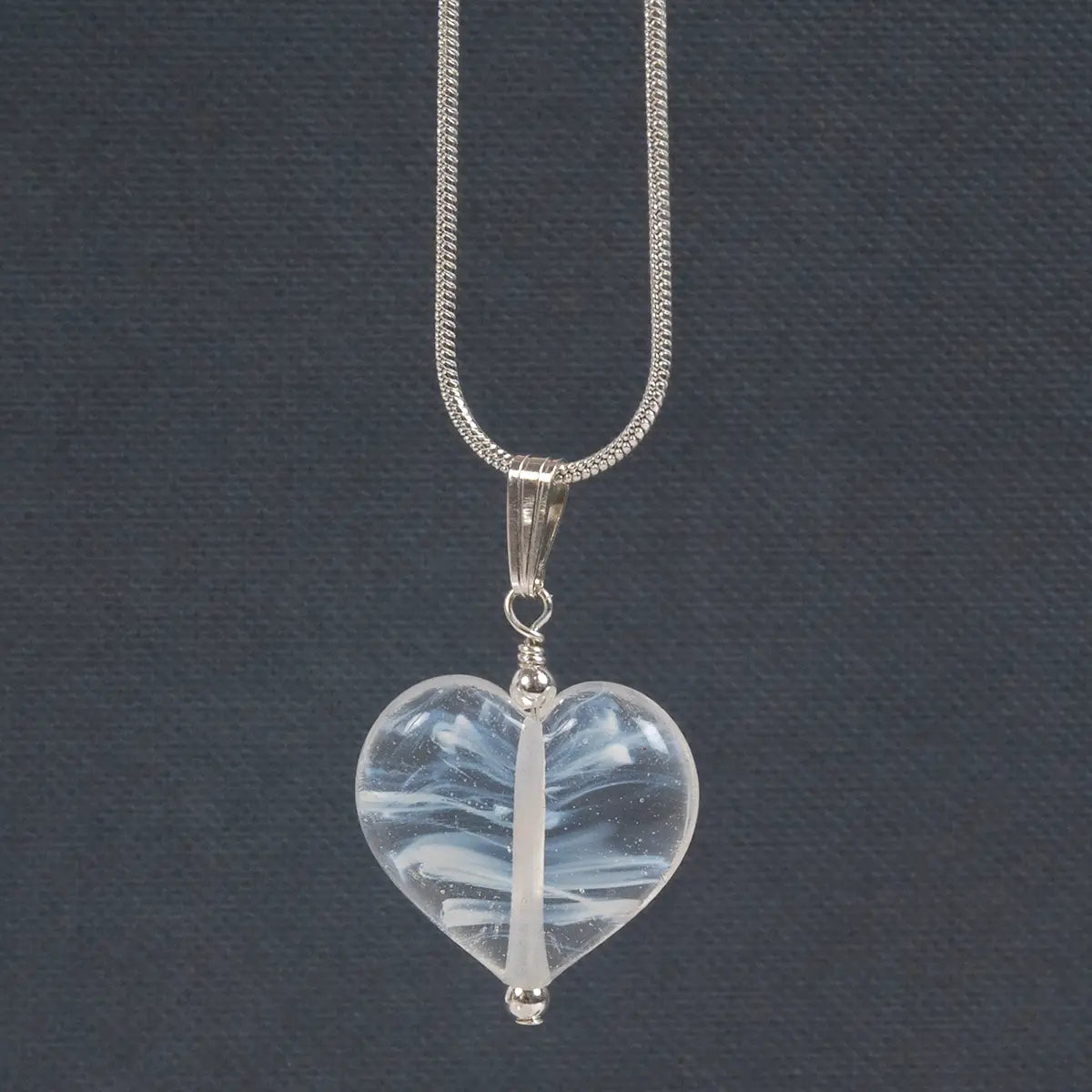 a white/clear glass heart on a silver chain against a dark grey backgrouond