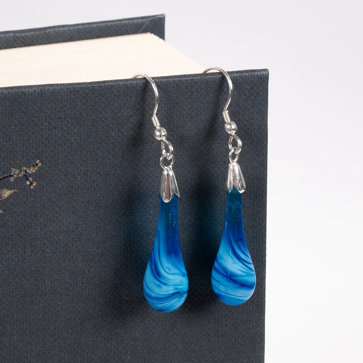blue glass drop earrings with silver details hanging from a book