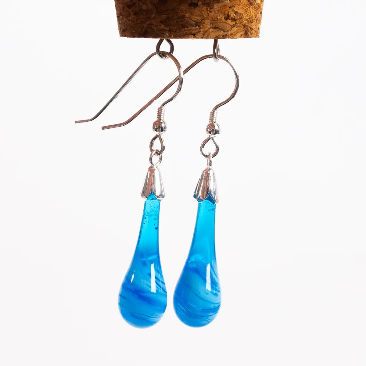 blue glass drop earrings against a white background, hanging from a cork with metal loops