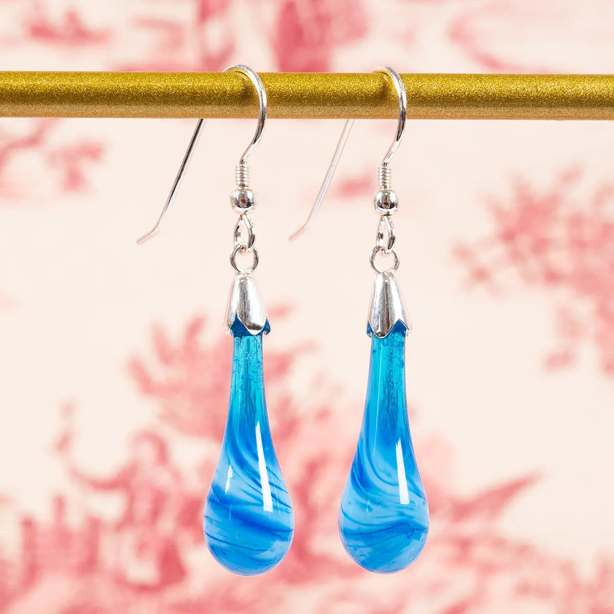blue glass earrings hanging from a gold bar against a red and cream background