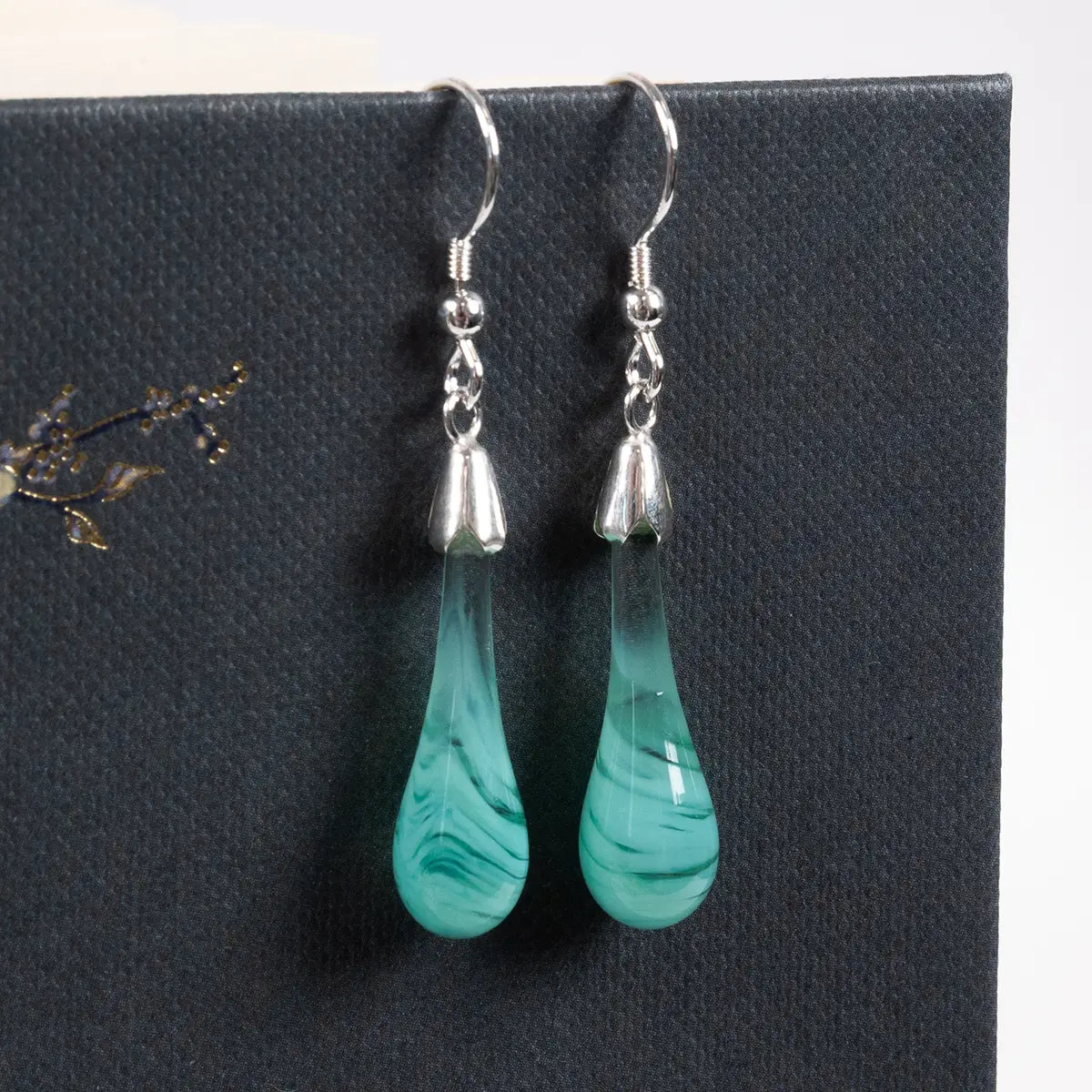 mint coloured drop earrings hanging from a book