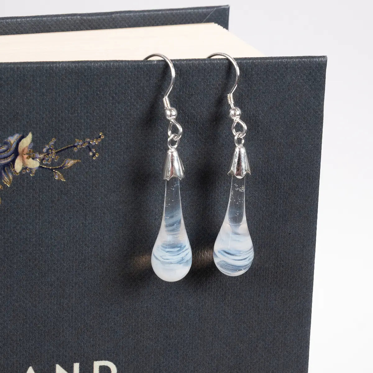 white glass drop earrings with silver details on a book