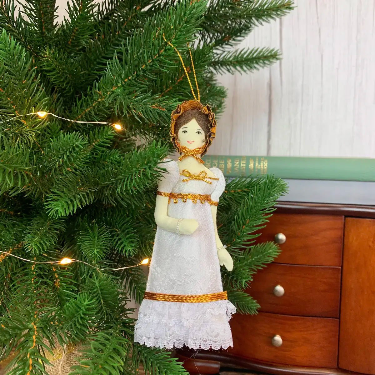 Elizabeth Lizzie Lizzy Bennet doll with hanging loop hanging as christmas decoration from christmas tree with lights against wooden background