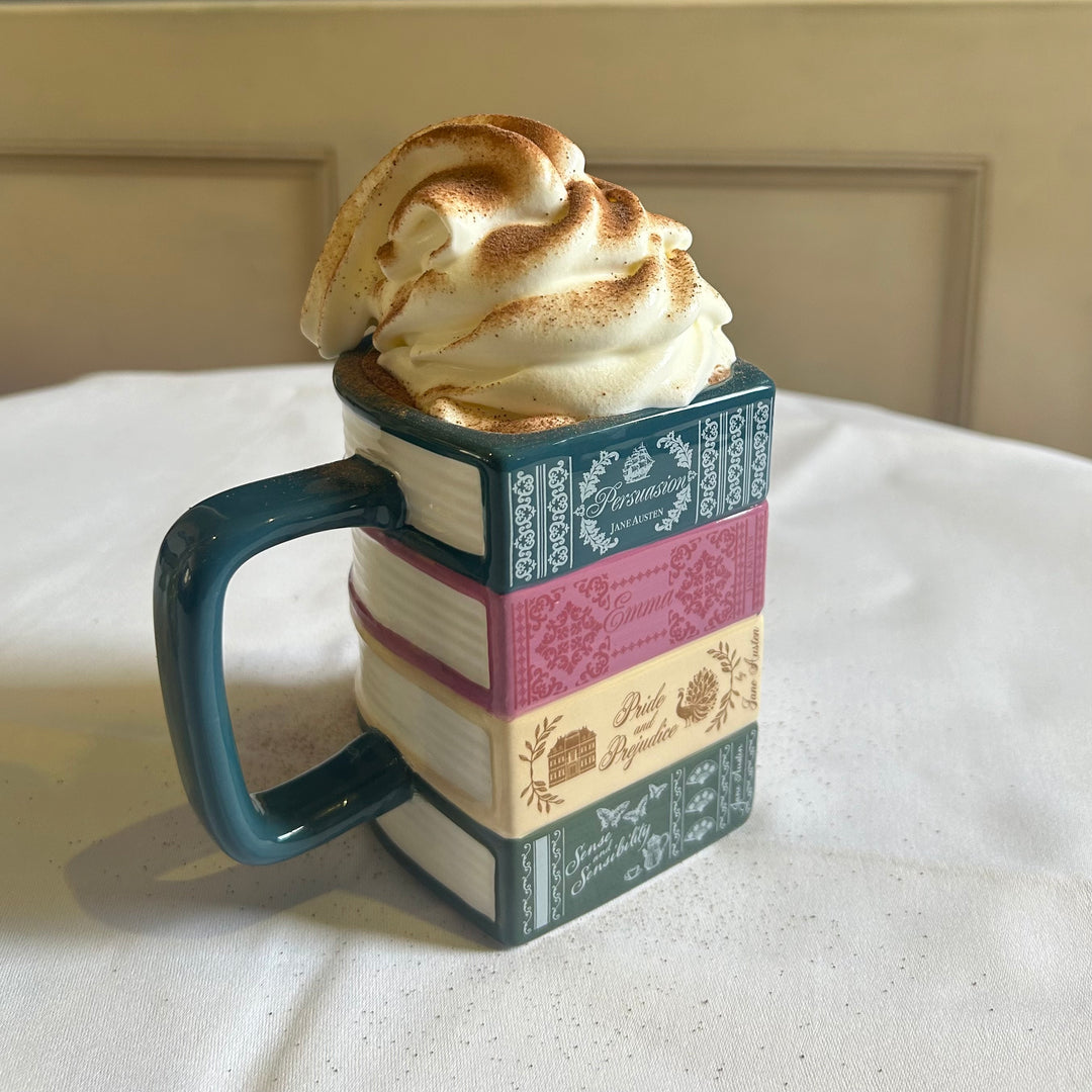 Video shows mug full of hot chocolate and marshmallows. Someone uses a whipped cream can and dusts the top with chocolate,
