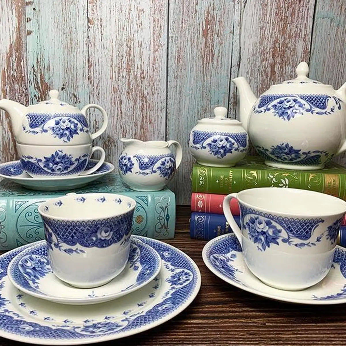 set of blue and white netherfield bone china teapots, teacups, teasets, saucers, and jugs on a wooden table against a wooden background stacked up on Jane Austen books in various hardcover editions