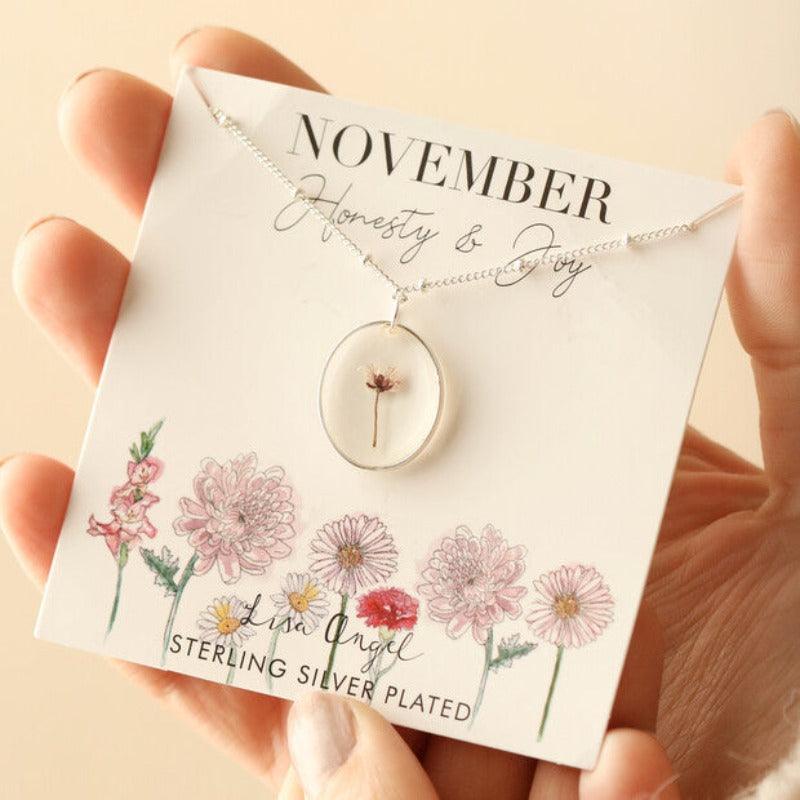 The November necklace is displayed on its jewellery card with illustrations of colourful flowers and the words 