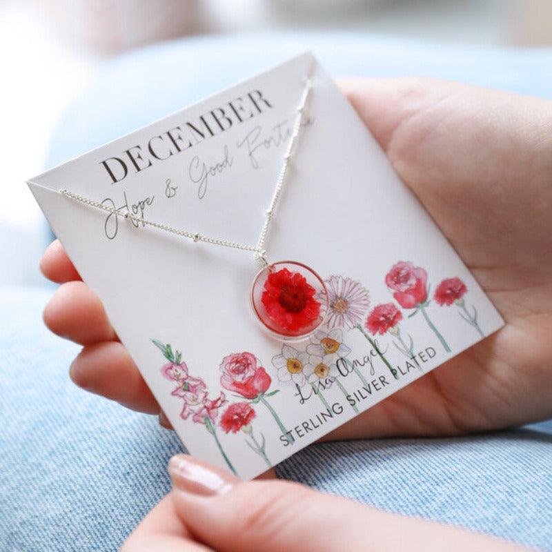 December Necklace is displayed on it's jewellery card. It is decorated with illustrated flowers and the words "hope and good fortune". The Flower is a strong red colour and is set in resin on a silver chain 