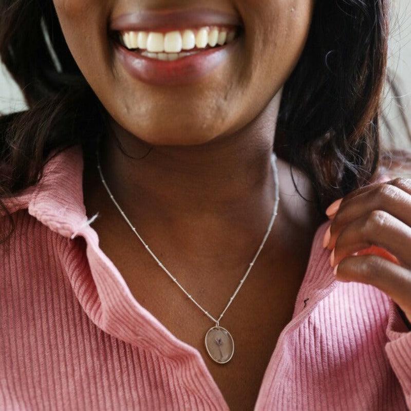 A woman wears the dainy november necklace around her neck. A tiny flower on a delicate stem is set in resin and hangs on a satellite silver chain