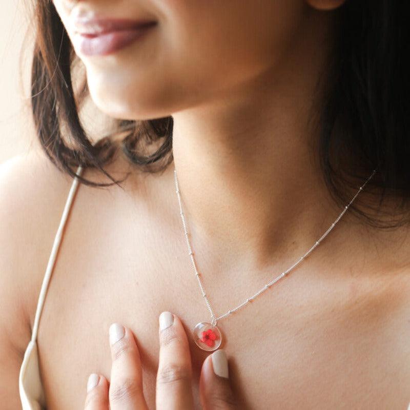 A lady wears the June necklace. It has a red flower set in resin hanging from a satellite silver chain. 