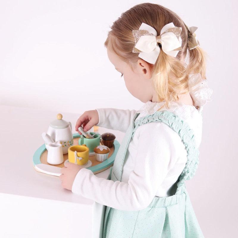 a little girl with bows in her hair is playing with the tet and is enjoying stirring the teacup. 