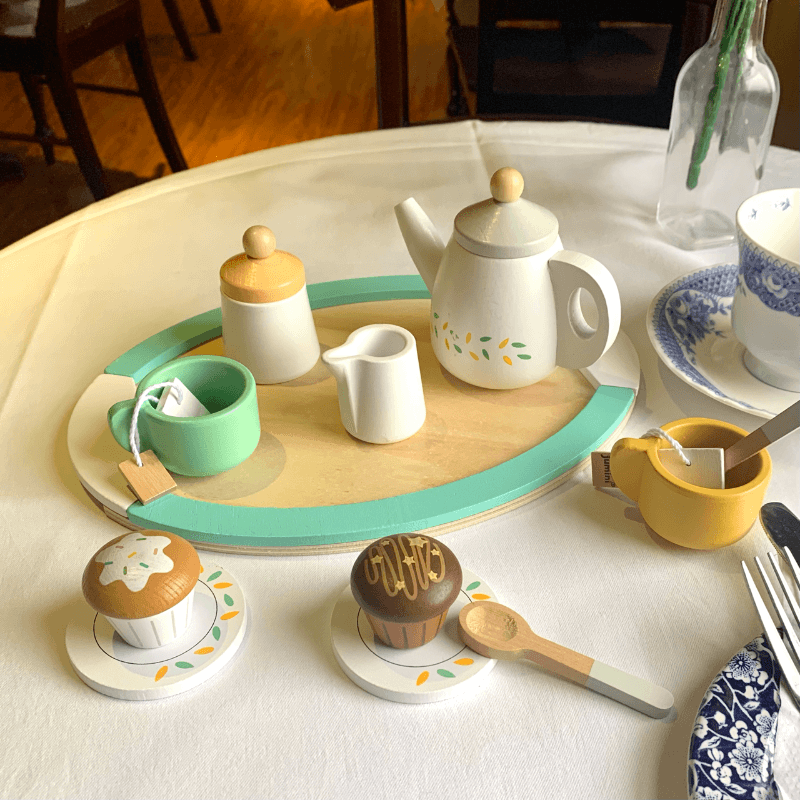 The cute tea set is shown here on on a table with a clean white table cloth. the lovely set is shown with the painted teaspoons and tray shown in the sunlight. 